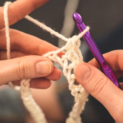 Crochet tools | image shows a person crocheting with some white yarn and a purple crochet hook | Yarn Worx