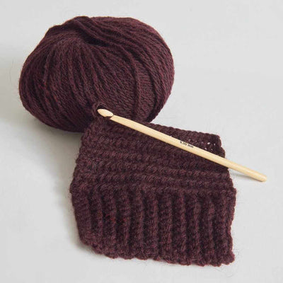 Knitted brown fabric with a wooden crochet hook and yarn ball on a light gray background | Yarn Worx