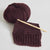 Knitted brown fabric with a wooden crochet hook and yarn ball on a light gray background | Yarn Worx