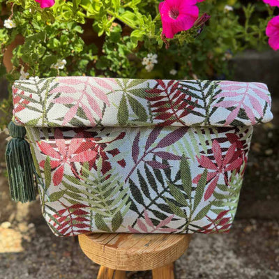 Floral-patterned fabric basket with tassels on a wooden stand, surrounded by pink flowers.