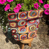 Colorful patterned bag on a wooden stand with pink flowers in the background