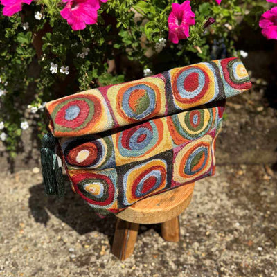 Colorful patterned fabric project bag on a wooden stool with flowers in the background
