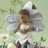 Crocheted fairy with grey wings and brown hair holding flowers, surrounded by greenery | Yarn Worx