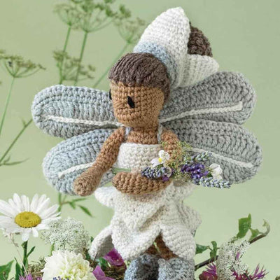 Crocheted fairy with grey wings and brown hair holding flowers, surrounded by greenery | Yarn Worx
