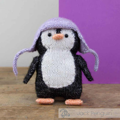 Knitted penguin toy with a purple hat on a wooden surface with a purple and gray background | Yarn Worx