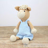 Crocheted alpaca toy wearing a blue outfit on a wooden surface with a white background | Yarn Worx