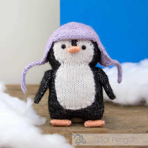 Knitted penguin toy with a purple hat on a wooden surface with snow-like material | Yarn Worx