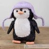 Knitted penguin toy with a purple hat on a wooden surface | Yarn Worx
