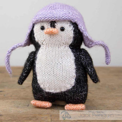 Knitted penguin toy with a purple hat on a wooden surface | Yarn Worx