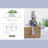 Knitted rhinoceros toy with a striped sweater on a wooden shelf, surrounded by plants | Yarn Worx