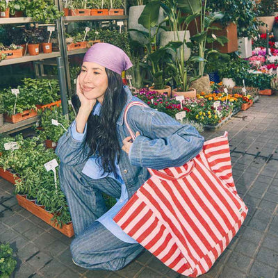 Woman sitting among plants and flowers with a red and pink striped bag | Yarn Worx