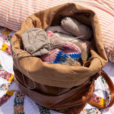 Brown bag filled with yarn and knitting materials on a colourful fabric background | Yarn Worx