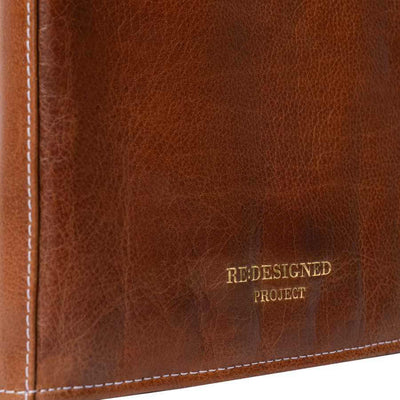 Close-up of a brown leather product corner with visible white stitching and gold embossed text reading 'REDESIGNED PROJECT' | Yarn Worx