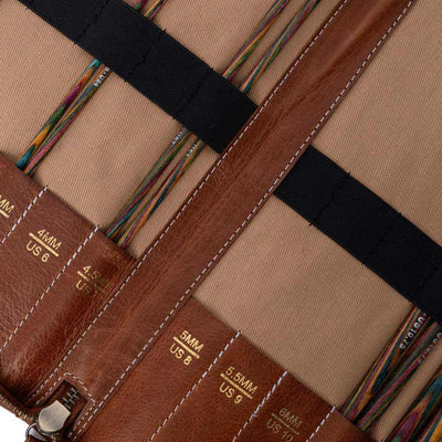Close-up of a leather tool roll with various sizes of needles inside, on a beige background | Yarn Worx