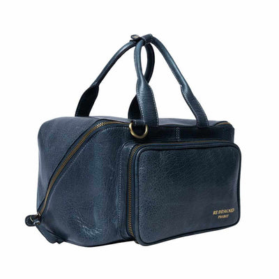 Re:Designed Project 39 Sapphire Blue leather travel bag with dual top handles, a front zippered pocket, and a diagonal zipper, shown on a plain white background.