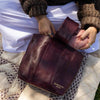 Person holding a maroon leather bag with yarn, sitting on a patterned blanket | Yarn Worx