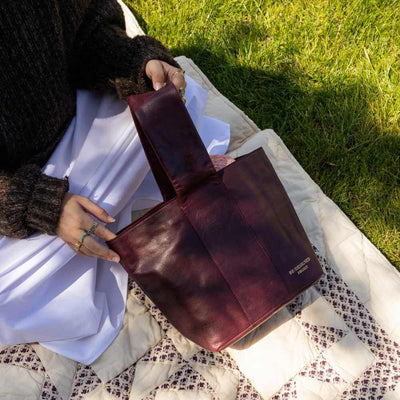 Person holding a burgundy leather bag outdoors on a blanket | Yarn Worx