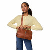 A woman wearing a pale yellow knit cardigan and blue jeans carries a brown leather shoulder bag with a matching leather strap against a plain white background | Yarn Worx