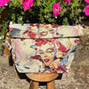 Floral and portrait-themed pouch on a wooden stand with flowers in the background