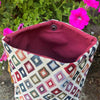 Multicolored geometric patterned bag with a purple interior against a floral background