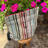 Striped fabric pouch with tassel on a wooden stool in front of pink flowers