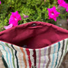 Multicolored striped bag with a red interior against a background of pink flowers.