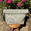 Patterned clutch bag with tassel on a wooden stool with flowers in the background