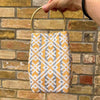 Handbag with geometric pattern held by a hand against a brick wall.
