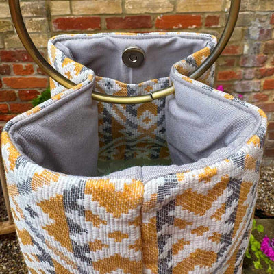 Patterned fabric bag with gold handle against a brick wall background