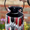 Decorative tea pot with a colorful pattern held by a hand against a blurred outdoor background.
