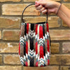 Handbag with a colorful zigzag pattern held by a hand against a brick wall.