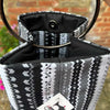 Black and white patterned handbag with a visible brand tag against a blurred outdoor background.