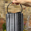 Hand holding a black and gray patterned woven bag against a blurred background