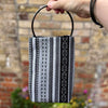 Hand holding a black and gray patterned bag against a brick wall background