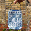 Blue patterned bag with a gold handle held in front of a brick wall.