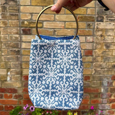 Blue patterned bag with a gold handle held in front of a brick wall.