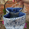 Blue and white patterned fabric bucket with a metal handle against a brick wall background.