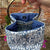 Blue and white patterned fabric bucket with a metal handle against a brick wall background.