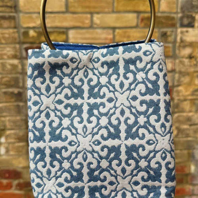 Blue patterned bag with gold handles against a brick wall background