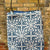 Blue patterned bag with gold handles against a brick wall background