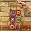 Colorful handbag with circular patterns held against a brick wall