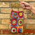 Colorful handbag with circular patterns held against a brick wall