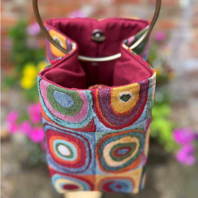 Colorful fabric pouch with a drawstring and handle against a blurred floral background