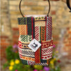 Colorful patterned bag with a brand tag against a blurred floral and brick wall background