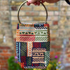 Colorful patterned bag with gold handle held by a hand against a blurred background