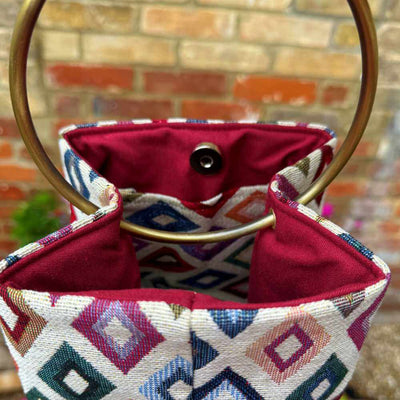 Decorative handbag with geometric pattern and gold handles against a brick wall.