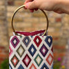 Handbag with geometric pattern held by a hand against a blurred brick wall background