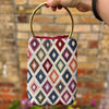 Handbag with geometric pattern held by a person against a brick wall.
