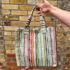 Multicolored striped tote bag held against a brick wall