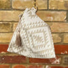 Small pouch with geometric pattern and tassel against a brick wall background